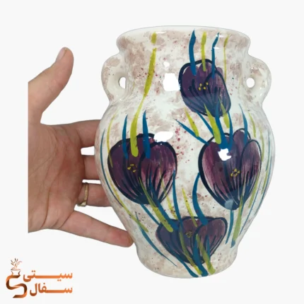 گلدان دیوارکوب کوزه‌ای بنفش در کنار دست برای درک اندازه