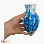 گلدان دیوارکوب قطره‌ای آبی مدل شبنم سرامیکی با گل‌های آبی روی زمینه‌ی آبرنگی آسمانی در دست برای ابعاد